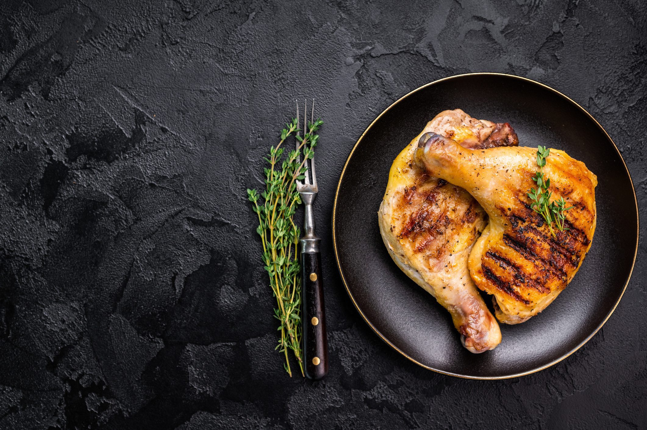 Grilled chicken leg on black plate with thyme